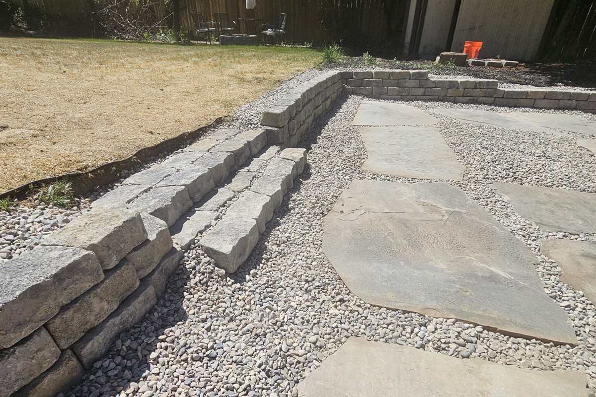 A finished retaining wall with built-in steps and a paver patio, built by Stauffer Custom Contracting